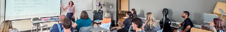 A woman speaks to students seated in a classroom during a presentation.