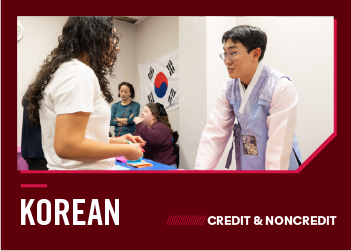 A young man wearing a traditional hanbok speaks with a student in front of a South Korean flag.
