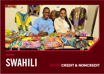 A man and a woman sit behind a table filled with colorful patterned African fabrics and clothing.
